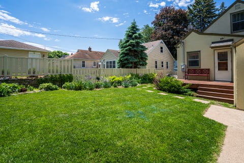 Backyard scene featuring a green lawn, flower beds, and a cozy house.