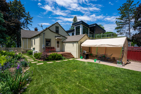 A backyard view featuring a yellow house, a modern home, and a shaded outdoor tent area.
