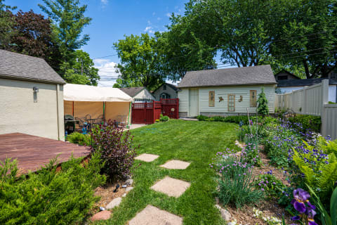 A tranquil backyard with a green lawn, flowers, a tent, and a shed under a blue sky.