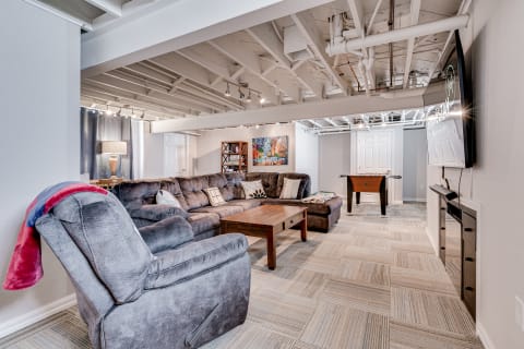 A modern basement living area featuring a sectional sofa, coffee table, foosball table, and muted lighting.