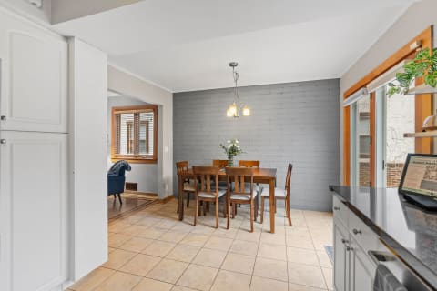 Modern dining area with a wooden table, grey brick wall, and natural light from a window.