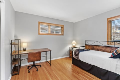 Cozy bedroom featuring a bed, desk, and warm wooden flooring.
