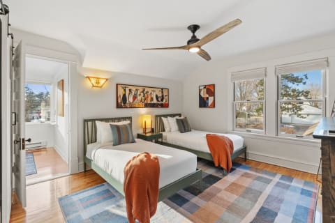 A bright twin bedroom with two beds, colorful decor, and natural light from large windows.