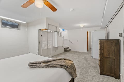 Spacious bedroom featuring a white bed, textured blanket, ceiling fan, and wooden dresser with carpeted flooring.