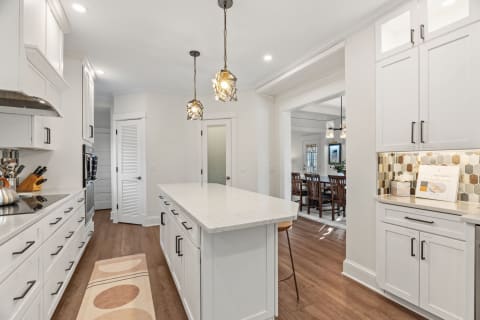 Modern kitchen with white cabinetry, pendant lights, and a large island.