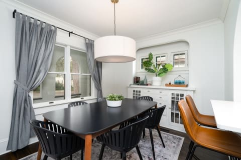 A modern dining room featuring a black table, gray curtains, and a white sideboard.