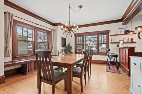 Dining area featuring a wooden table, modern chandelier, and large windows.