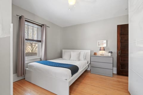 A modern bedroom featuring a bed, gray dresser, and natural light from a window.