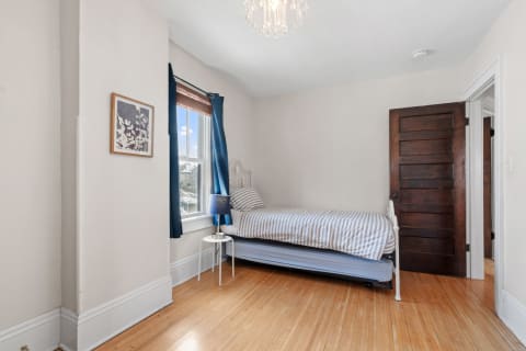 A small, cozy bedroom featuring a metal bed, blue curtains, and wooden flooring.