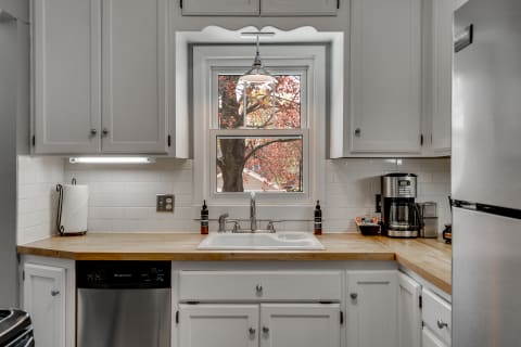Modern kitchen with white cabinets, farmhouse sink, and autumn view through window.