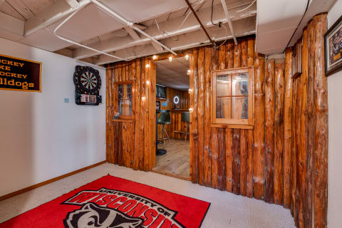 A rustic wooden entryway leads to a cozy basement area, highlighted by a dartboard and University of Wisconsin decor.