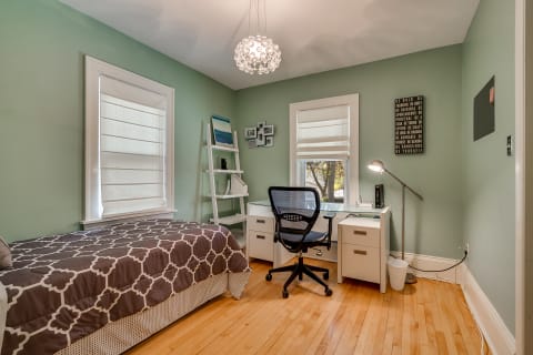 A cozy bedroom with a twin bed, a desk, and a chandelier, featuring green walls and wooden flooring.