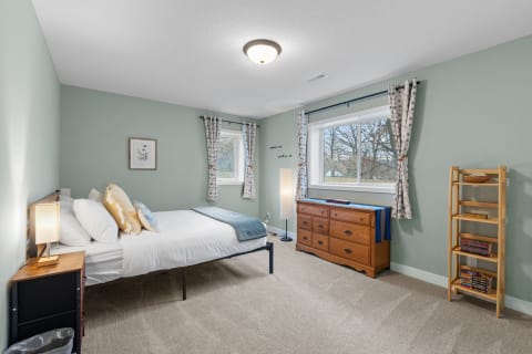A cozy bedroom featuring a bed with colorful pillows, a wooden dresser, and a tall shelf.