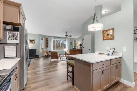 Contemporary kitchen with an open living area featuring large windows, a brown leather couch, and wooden flooring.