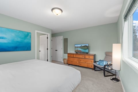 Serene bedroom with a cozy bed, abstract blue painting, and wooden dresser with TV.