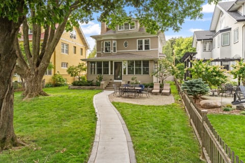A backyard featuring a traditional home surrounded by lush grass, with a winding path leading to a stone patio and outdoor seating.