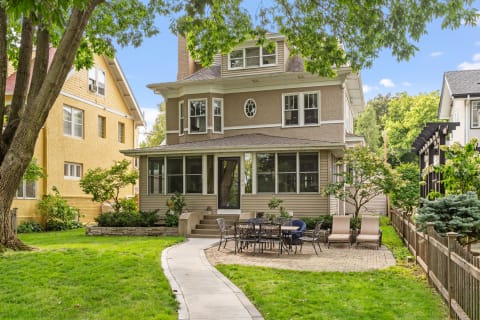 Two-story house with a porch and outdoor dining area in a green yard.