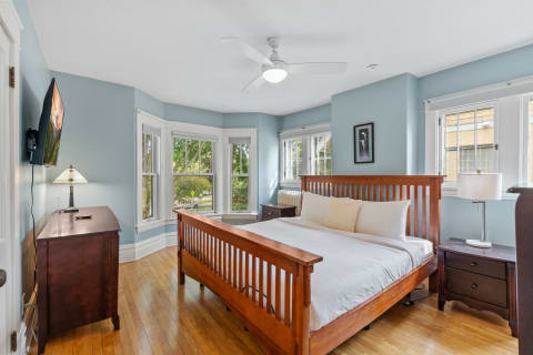 Bright bedroom featuring a wooden bed, light blue walls, and large windows.