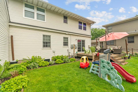 Backyard in a residential area featuring a deck, playground toys, and decorative plants.