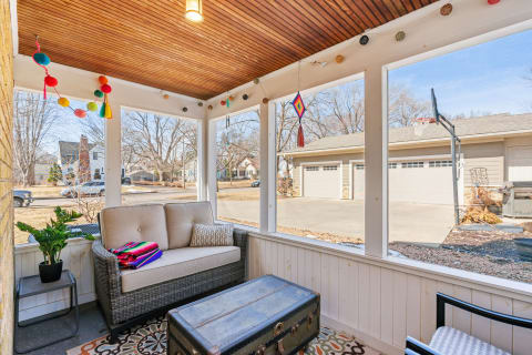 Cozy sunroom with beige couch, colorful blanket, and decorative garlands.