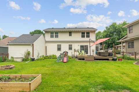 Suburban backyard with a cozy deck, playground slide, and garden bed.