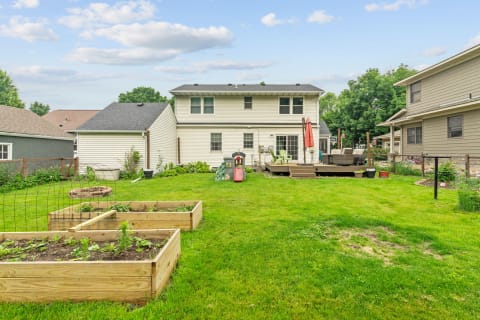 A backyard featuring garden beds and a deck with patio furniture.