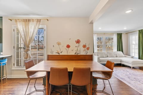 A dining area featuring a wooden table, leather chairs, and a flower accent wall with a view outside.