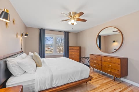 Cozy bedroom featuring a bed with white linens, wooden furniture, and large windows.
