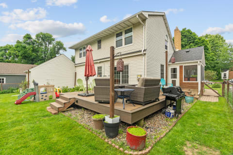Suburban backyard featuring a wooden deck with seating, plants, and a children's playset.