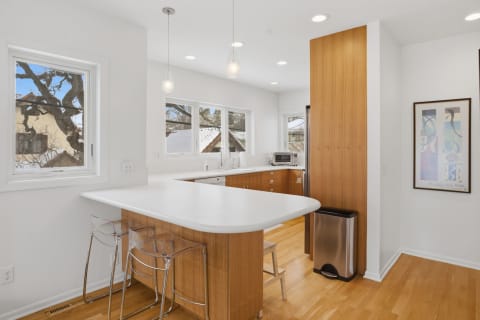Modern kitchen with wood cabinetry, white countertops, and bright windows.