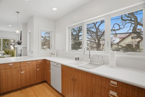 Modern kitchen with sleek wood cabinetry and bright white countertops, illuminated by natural light.