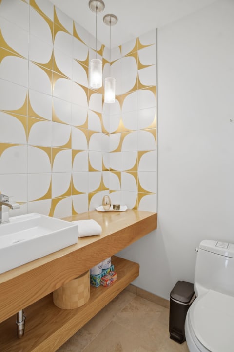 Modern bathroom featuring geometric gold and white tiles, a wood vanity, and pendant lighting.