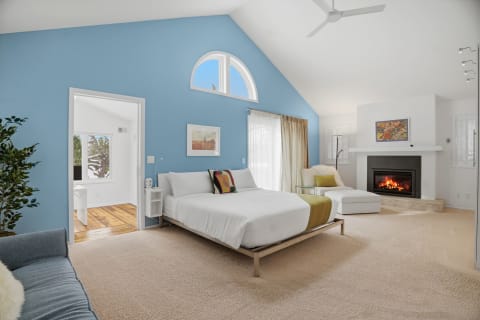 A spacious master suite featuring a king-sized bed, a cozy fireplace, and a vaulted ceiling with blue accents.