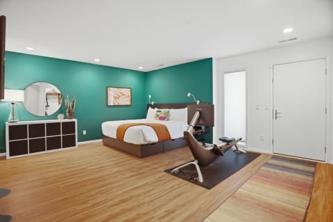 Interior view of a contemporary bedroom with a teal wall, large bed, and ergonomic chair.