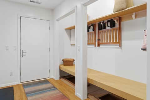 A bright entryway with a white door, wooden bench, and hooks on the wall.