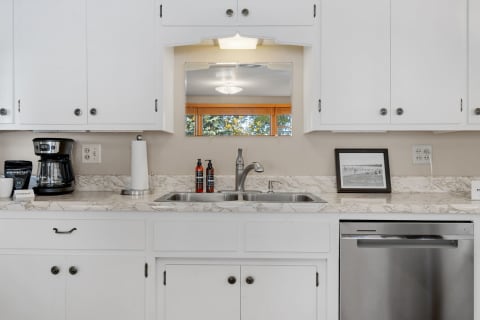 A clean kitchen with white cabinets and marble countertops, showcasing a sink, coffee maker, and framed photo.