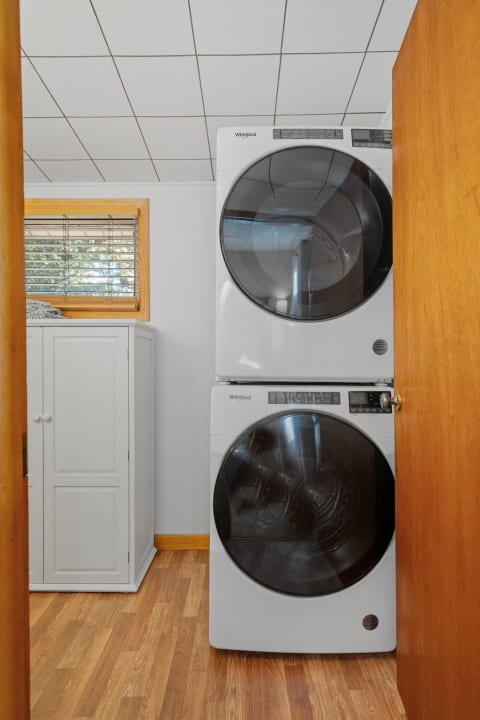 View of a laundry room with a stacked white washer and dryer next to a white cabinet and a window.