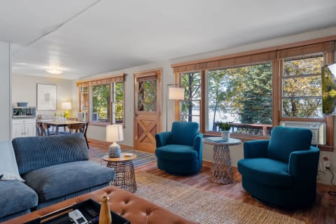 A cozy living room with teal chairs, a coffee table, and a view of a lake through large windows.