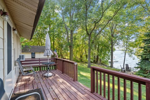Wooden deck overlooking a lake, with chairs, a table, and lush greenery.