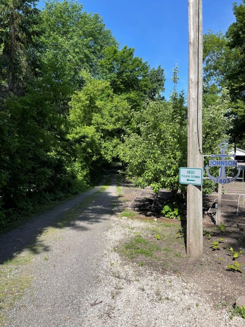 Tree-lined gravel pathway with signs indicating locations.