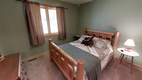 A rustic-themed bedroom with a wooden bed featuring animal carvings, a patterned quilt, and a window with brown curtains.