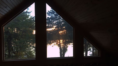 Interior view of a triangular window showing trees and a sunset.