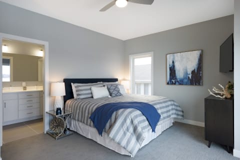 A modern bedroom featuring a king-sized bed with gray and white bedding, a bedside lamp, and abstract wall art.
