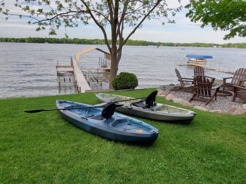 Two colorful kayaks on green grass next to a calm lake and wooden dock.