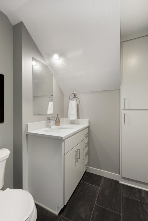 Modern bathroom with white vanity, gray walls, and dark tile flooring.