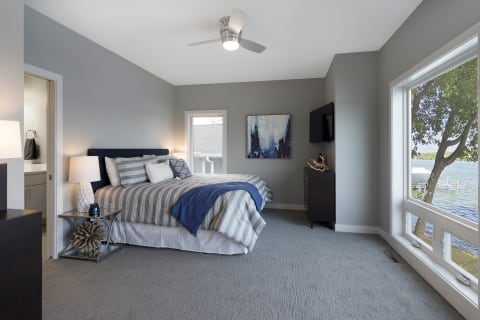 A modern bedroom featuring a large bed, soft lighting, a lake view through large windows, and contemporary decor.