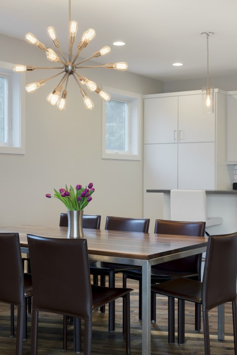 Modern dining room featuring a wooden table, dark leather chairs, and a stylish chandelier.