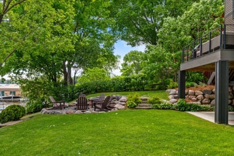 Outdoor space featuring wooden chairs and a fire pit surrounded by greenery.