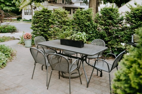 Outdoor dining table with chairs and a planter filled with herbs, surrounded by greenery.