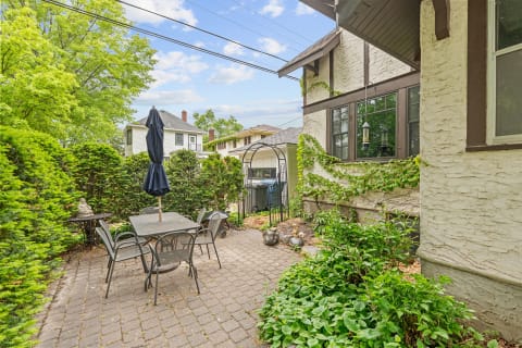 Outdoor patio area with a table and chairs, surrounded by greenery.